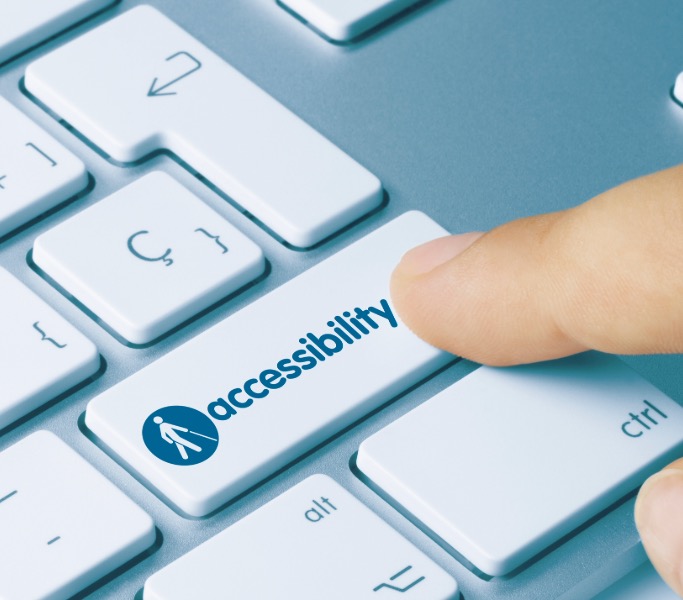 A finger pressing the "accessibility" key on a computer keyboard, symbolized with a wheelchair icon, emphasizing technology accessibility features.